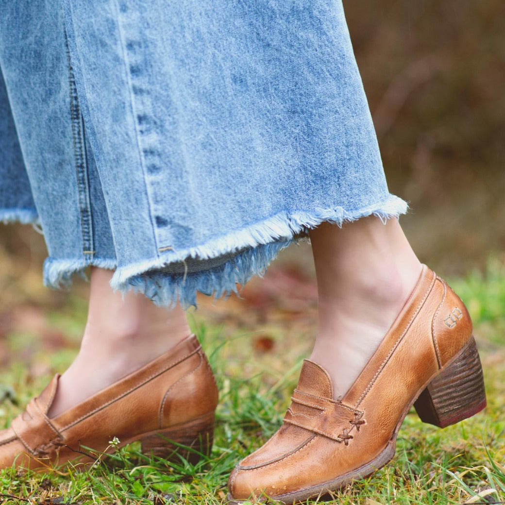 A woman wearing denim jeans and a pair of brown Bed Stu Liberty loafers.