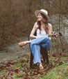 A woman wearing a Liberty hat and jeans sitting on a chair near a river.