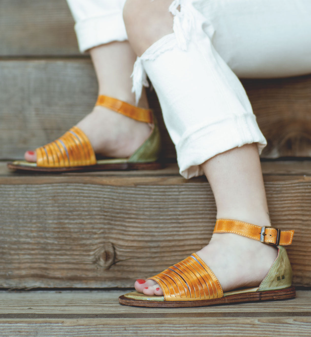 A woman wearing a pair of Bed Stu Lilia sandals on wooden steps.