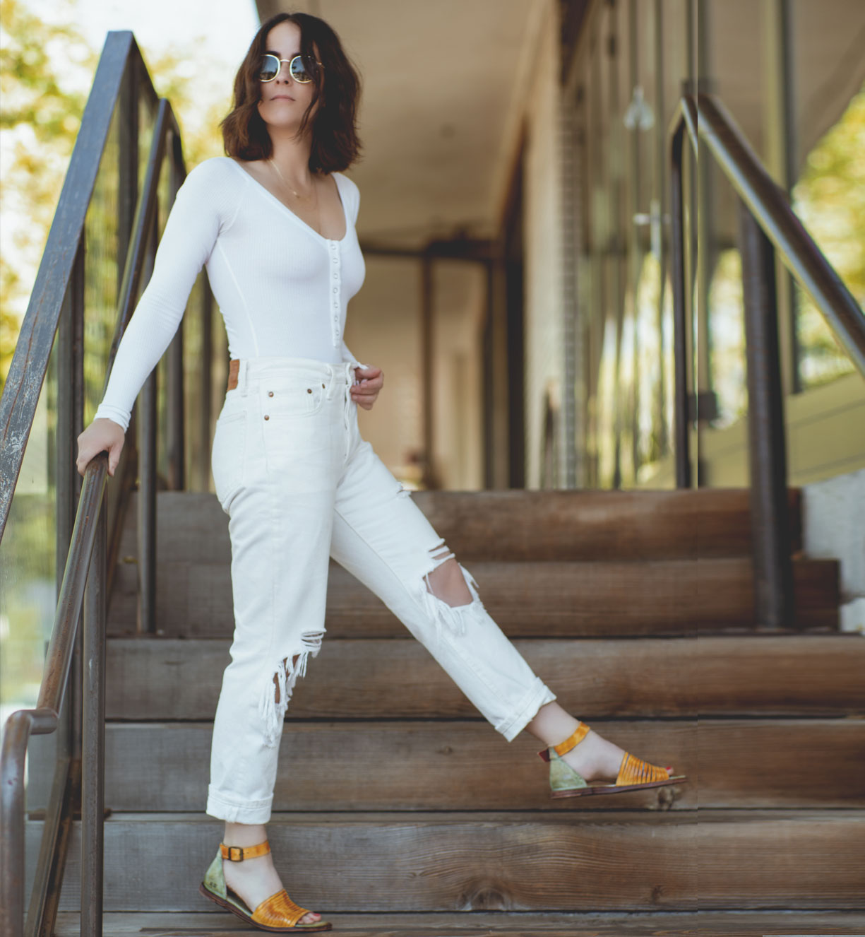 A woman wearing white Bed Stu jeans and Bed Stu sandals on stairs.