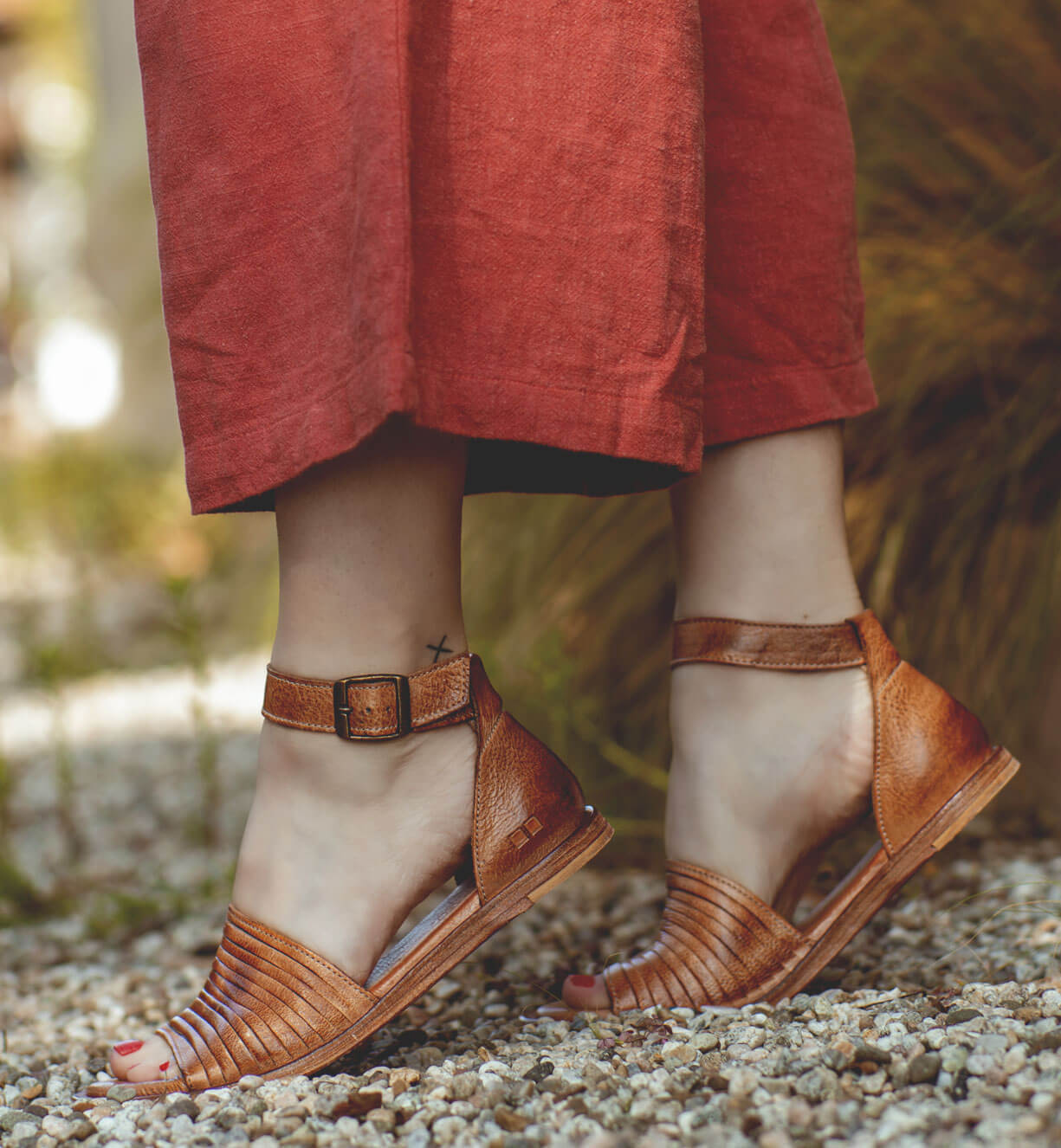 A woman wearing Bed Stu Lilia sandals standing on gravel.