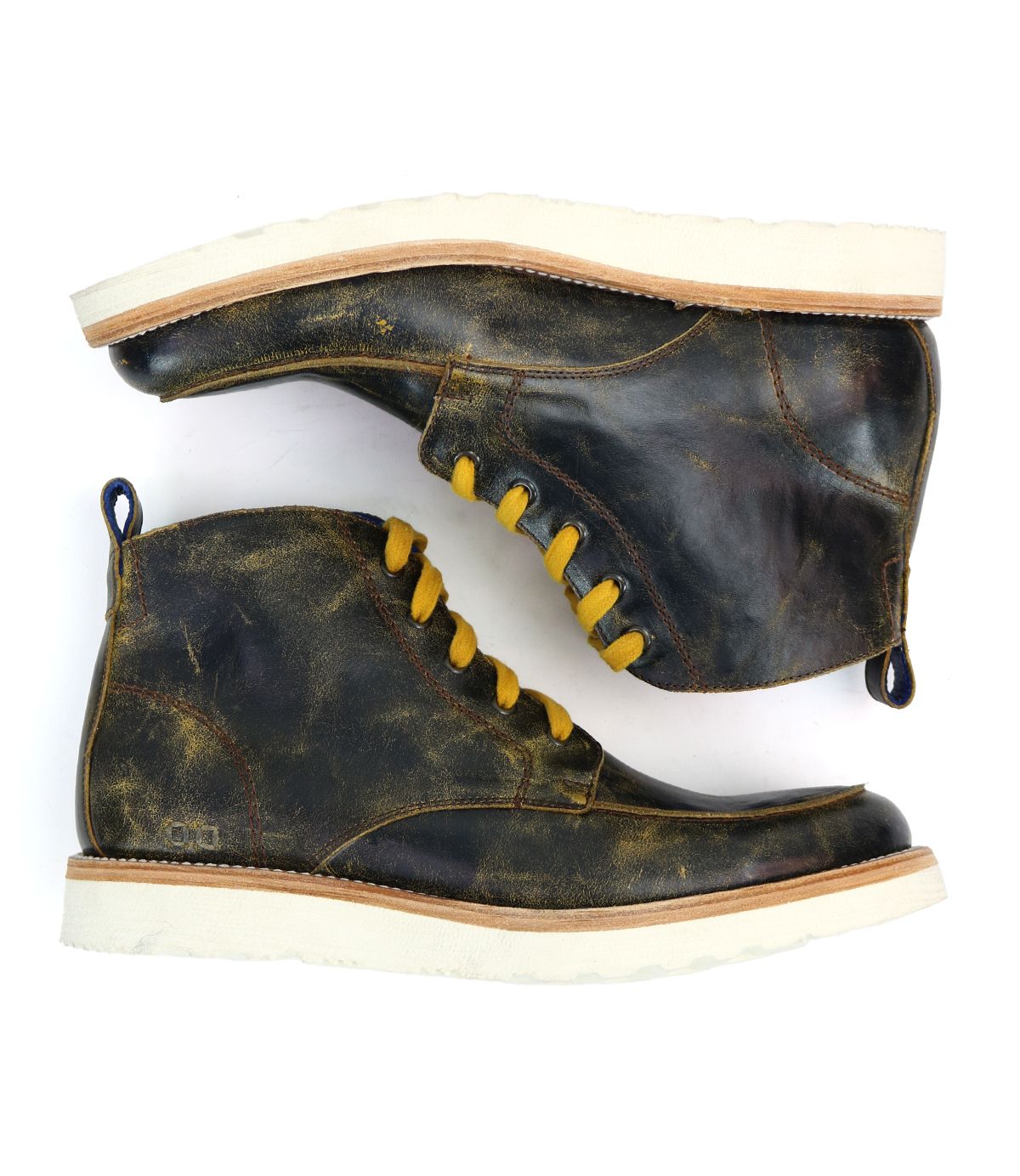 A top-down view of the Lincoln men's leather ankle boots, showcased with one boot resting on the other. Designed by Bed Stu, these well-worn, dark brown boots feature yellow laces, cream-colored soles, and practical heel loops, giving off a laid-back male aesthetic.