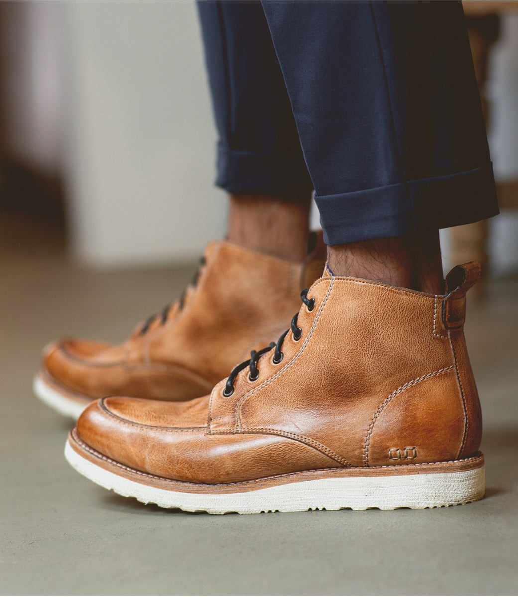 A man wearing brown Bed Stu men's leather boots and navy trousers, standing on a concrete floor.