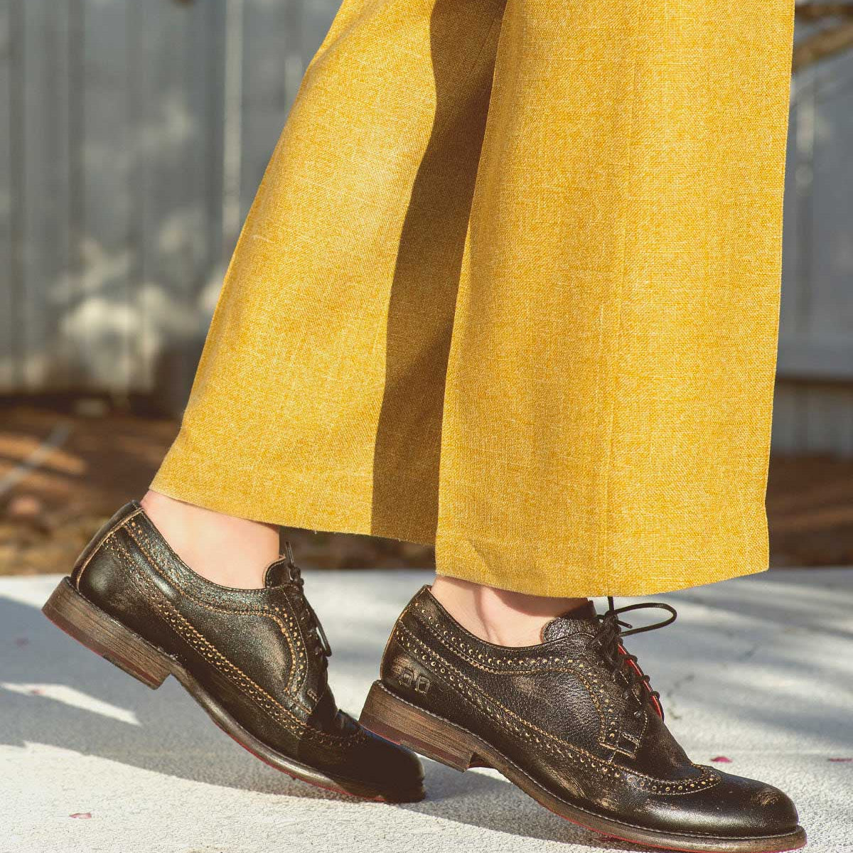 A woman wearing yellow pants and a pair of black Bed Stu Lita K II oxford shoes.