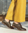A woman wearing yellow pants and a pair of black Bed Stu Lita K II oxford shoes.