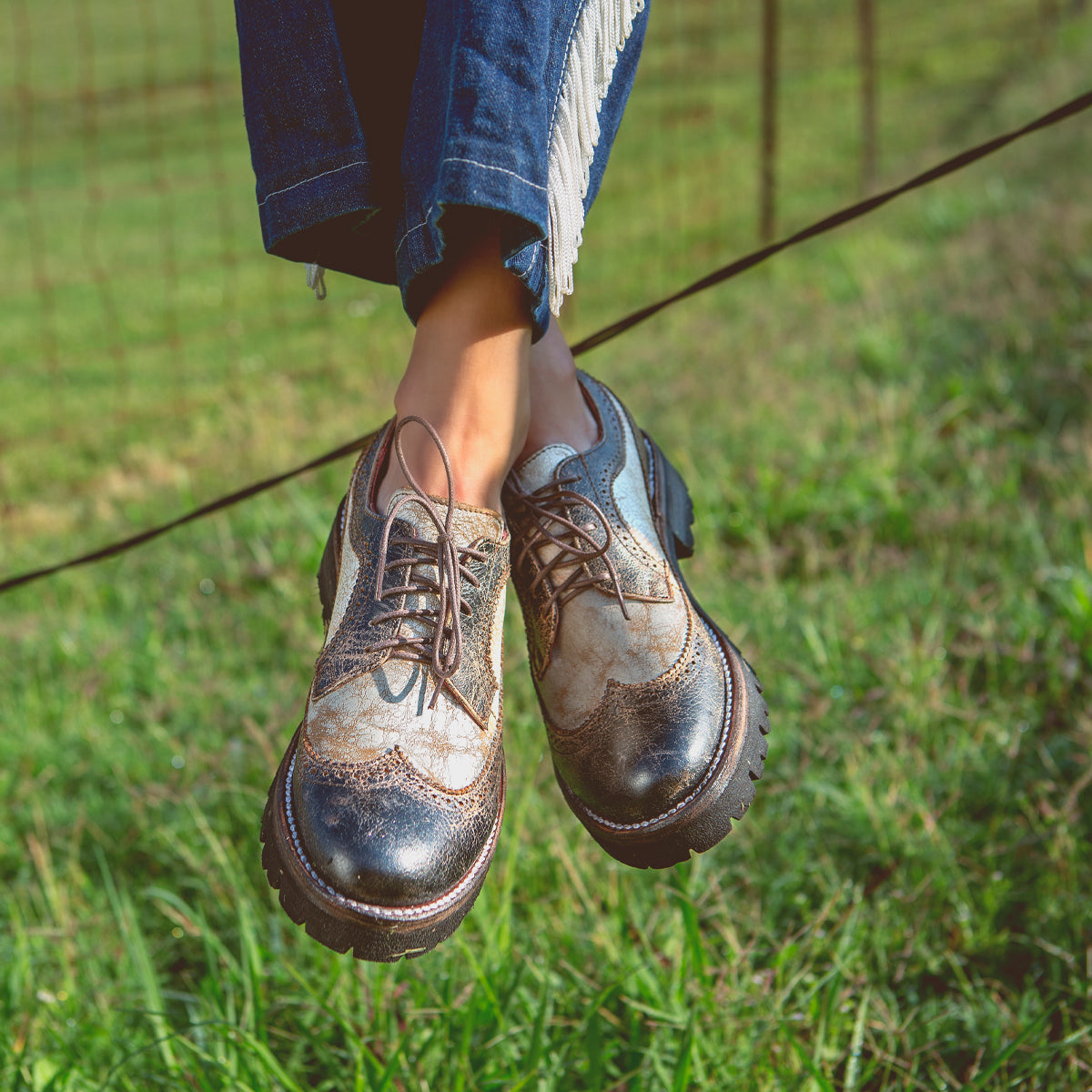 A woman sitting on a fence in a field wearing the Bed Stu Lita K III.