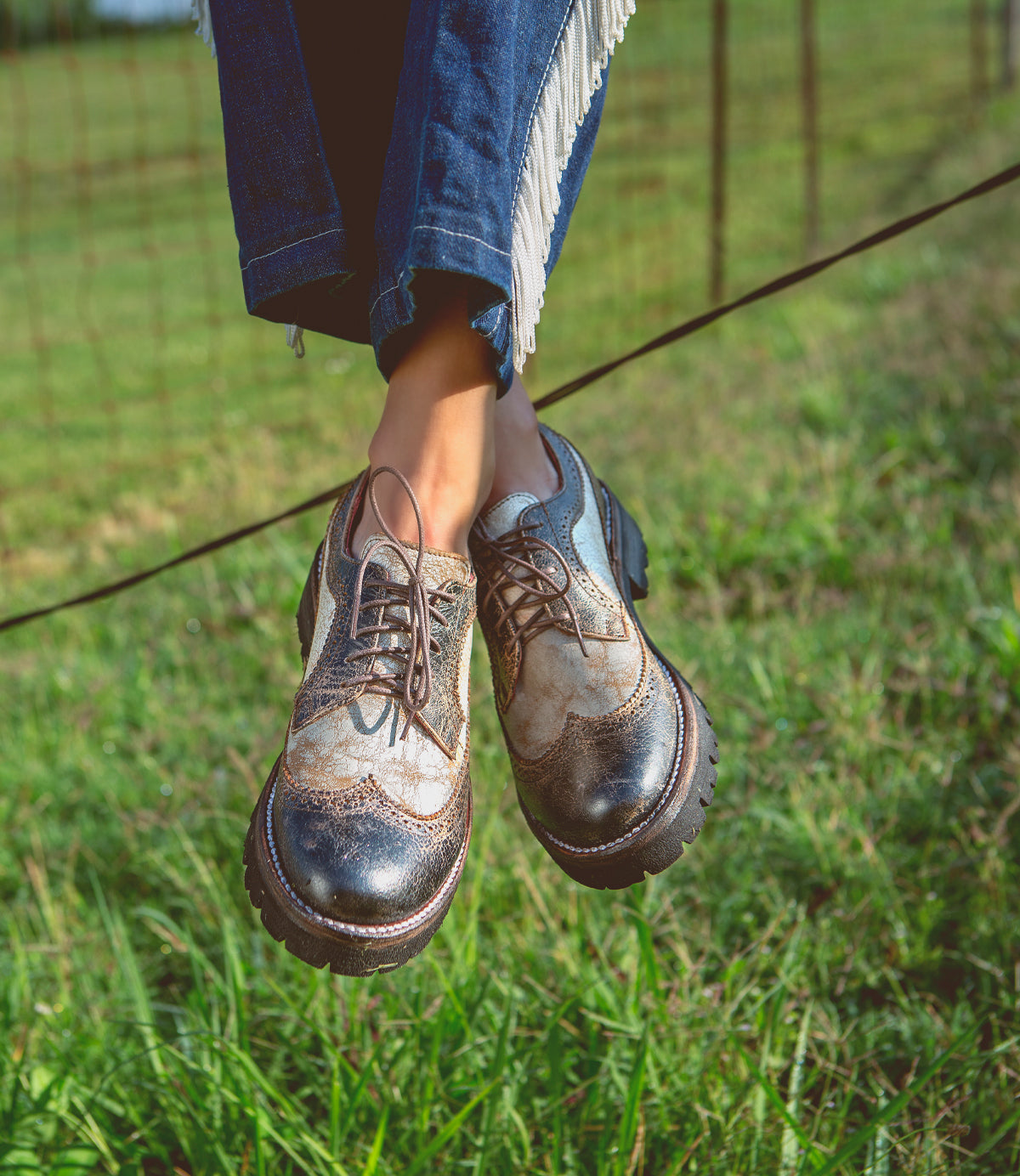 A woman sitting on a fence in a field wearing the Bed Stu Lita K III.