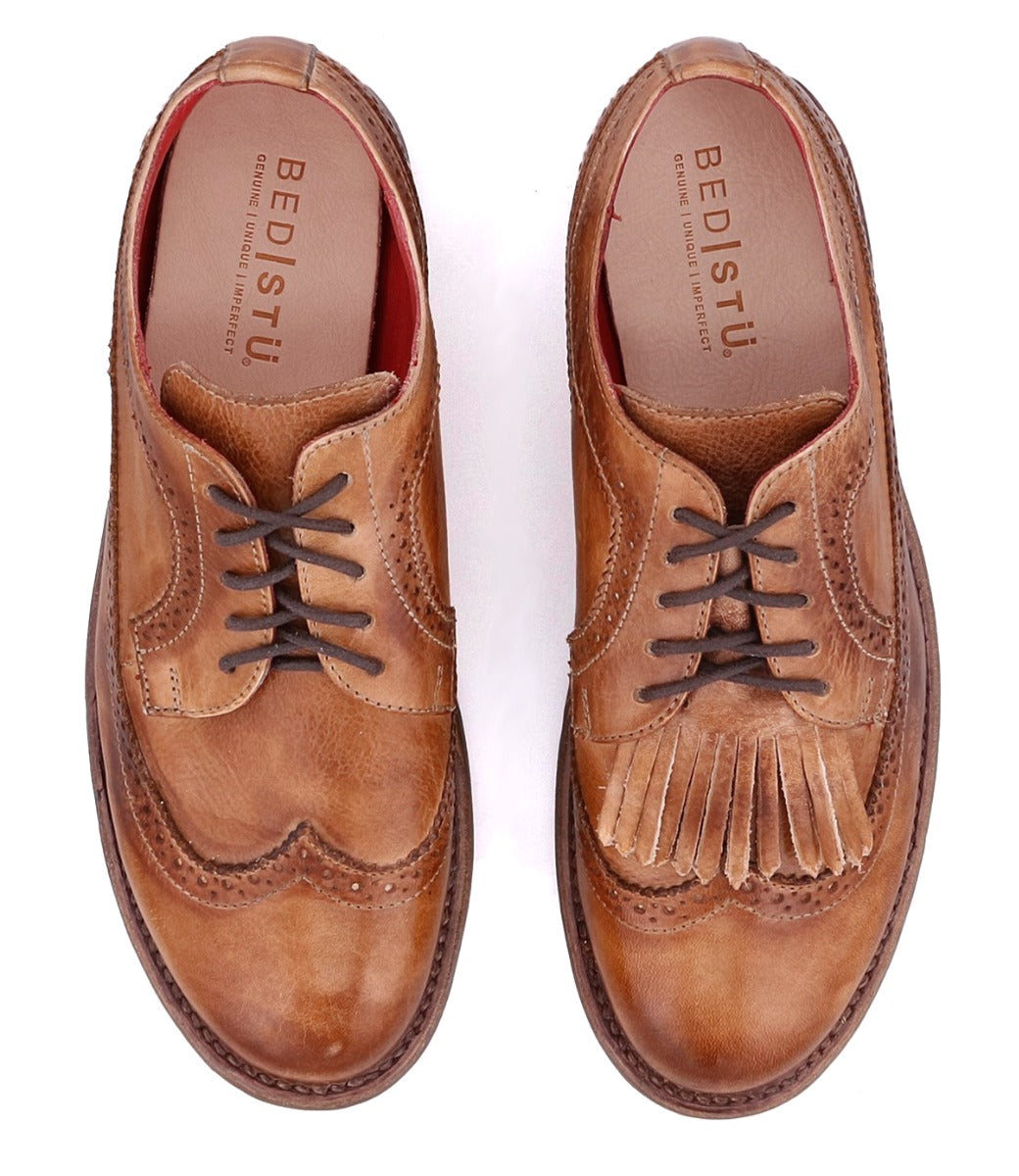The Bed Stu Lita K features brown leather construction; the left shoe has standard laces, while the right includes a removable kiltie with decorative fringe under the laces.