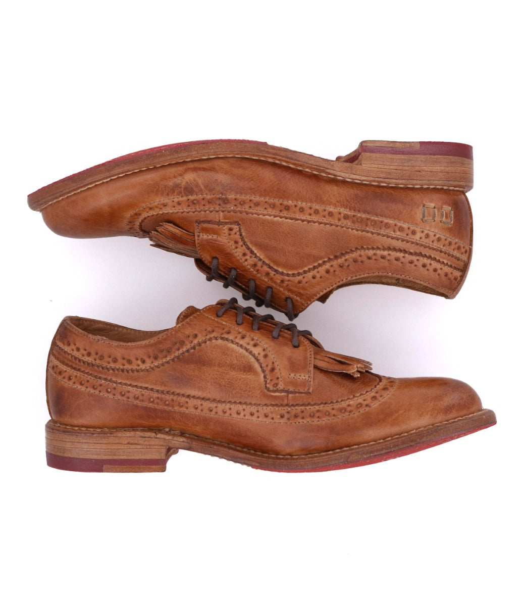 The Bed Stu Lita K is a pair of tan leather classic derby shoes with wingtip detailing, decorative perforations, stacked wooden soles, and red heel accents, displayed side by side on a white background.