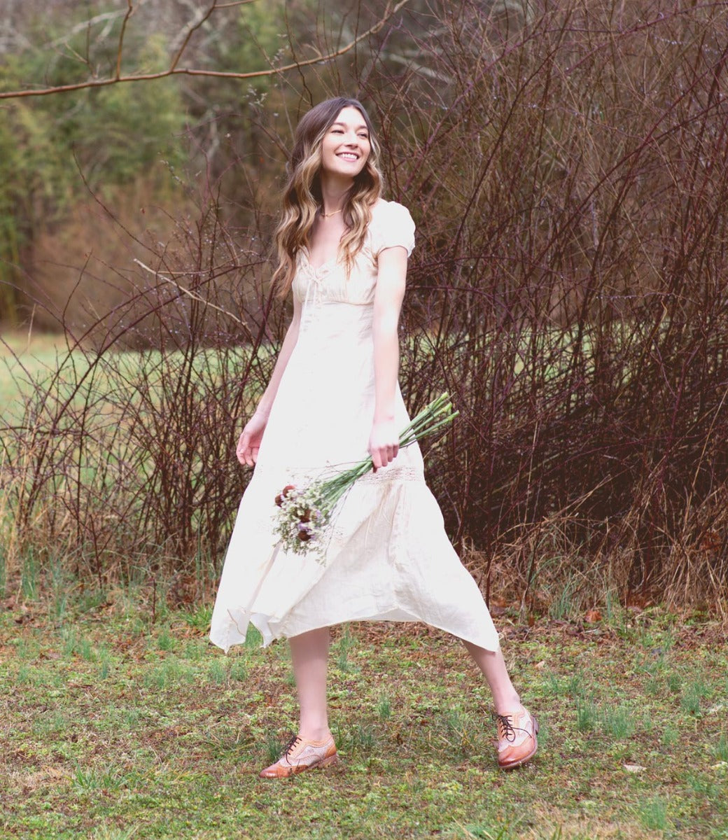 A woman in a white dress is standing in a field wearing Lita shoes by Bed Stu.