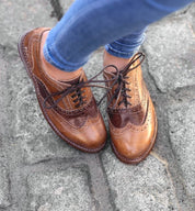 A woman wearing a pair of brown Wingtip Oxford shoes called Lita by Bed Stu.