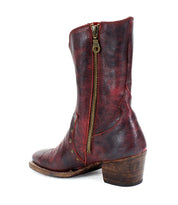 The "Locate" boot by Bed Stu is crafted from red leather, featuring flame-like stitching, a gold side zipper, and a wooden block heel.
