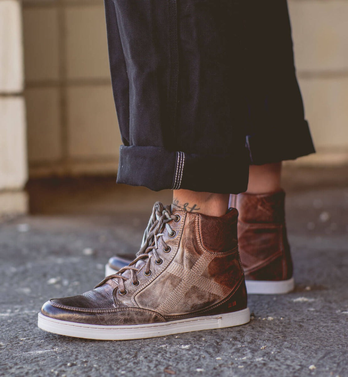 A person wearing a pair of brown Bed Stu Lordmind high top sneakers.