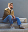 A man sitting on steps wearing a Bed Stu jacket and jeans.
