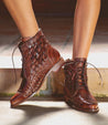 A woman's legs in a pair of Bed Stu Loretta brown woven ankle boots.