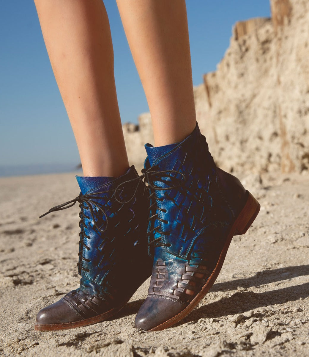 A woman wearing a pair of blue lace up Bed Stu Loretta boots on the beach.