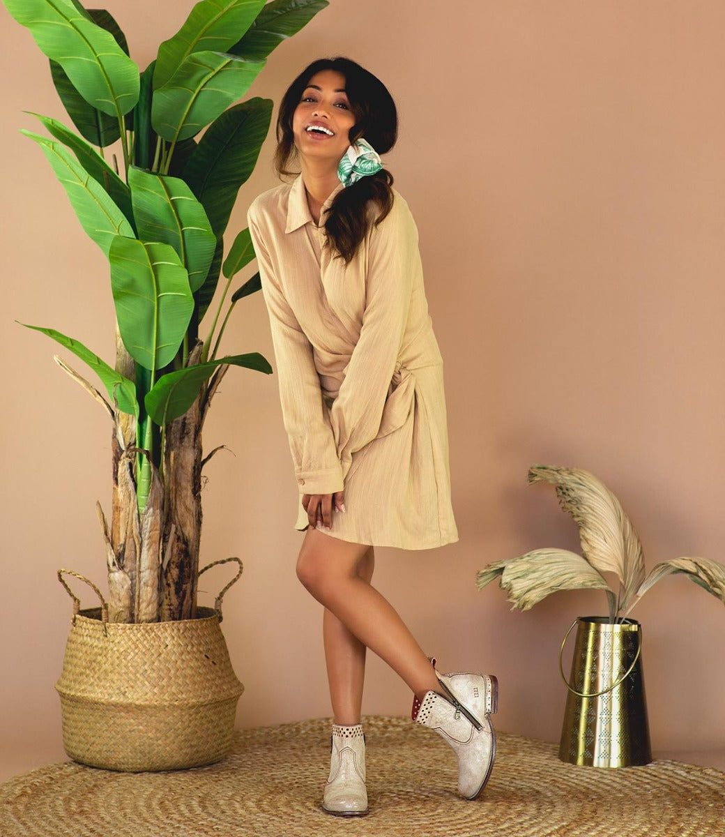 A woman in a tan shirt dress posing wearing Bed Stu Lotus boots.