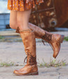 A woman wearing Loxley boots by Bed Stu and an orange dress.