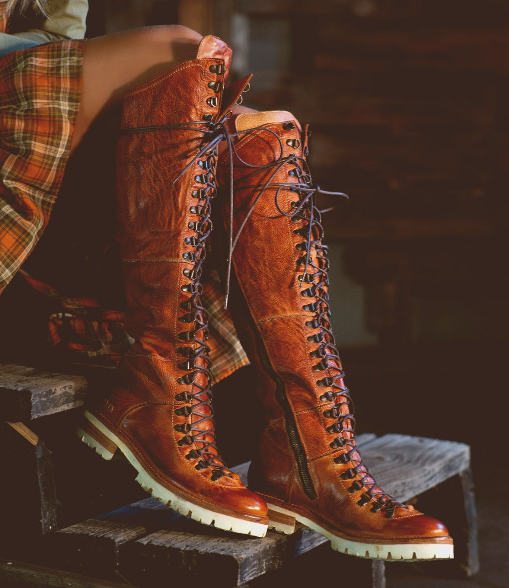A woman in a plaid shirt is wearing a pair of Bed Stu Lustrous boots.