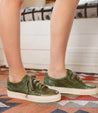 A woman wearing green Bed Stu Lyne sneakers on a rug.