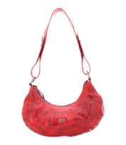 The Madre by Bed Stu is a red leather shoulder bag featuring a distinct crescent shape and adorned with metal studs, capturing a rock ‘n’ roll vibe. It includes a zip closure and adjustable strap, making it an edgy statement piece for any outfit.