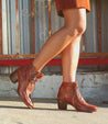 Close up of woman wearing distressed red ankle boots on street.