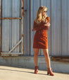 A blonde woman in a red dress and distressed red ankle boots while posing in front building.