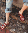 A woman's feet in Bed Stu Manati II sandals standing on a stone wall.