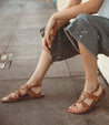 A woman wearing Bed Stu Manati II sandals sitting on a sidewalk.