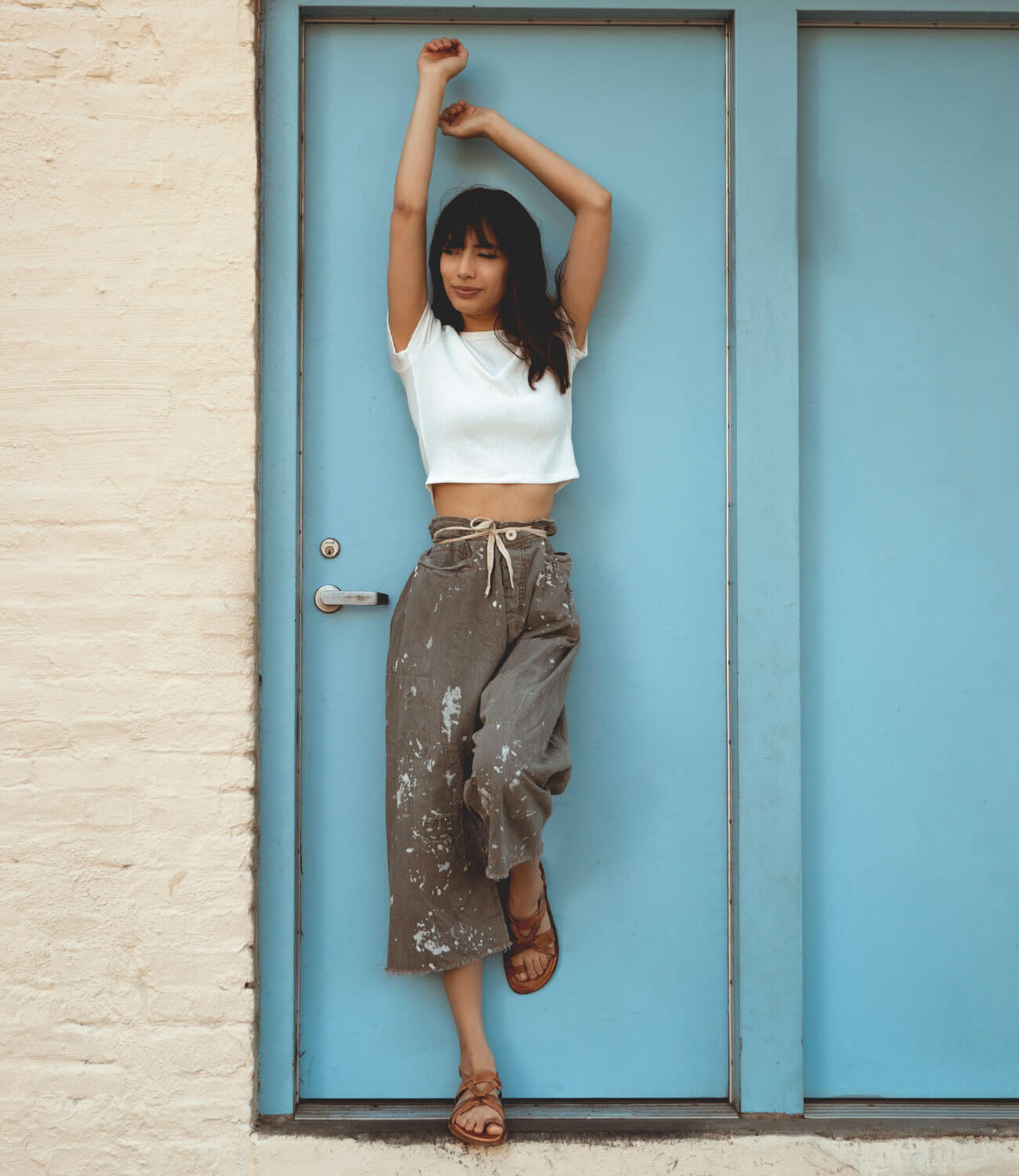 A woman leaning against a blue Bed Stu door, wearing the Manati II.