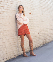 A woman is leaning against a brick wall wearing a Bed Stu Manchester III sweater and boots.