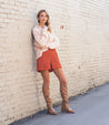 A woman is leaning against a brick wall wearing a Bed Stu Manchester III sweater and boots.