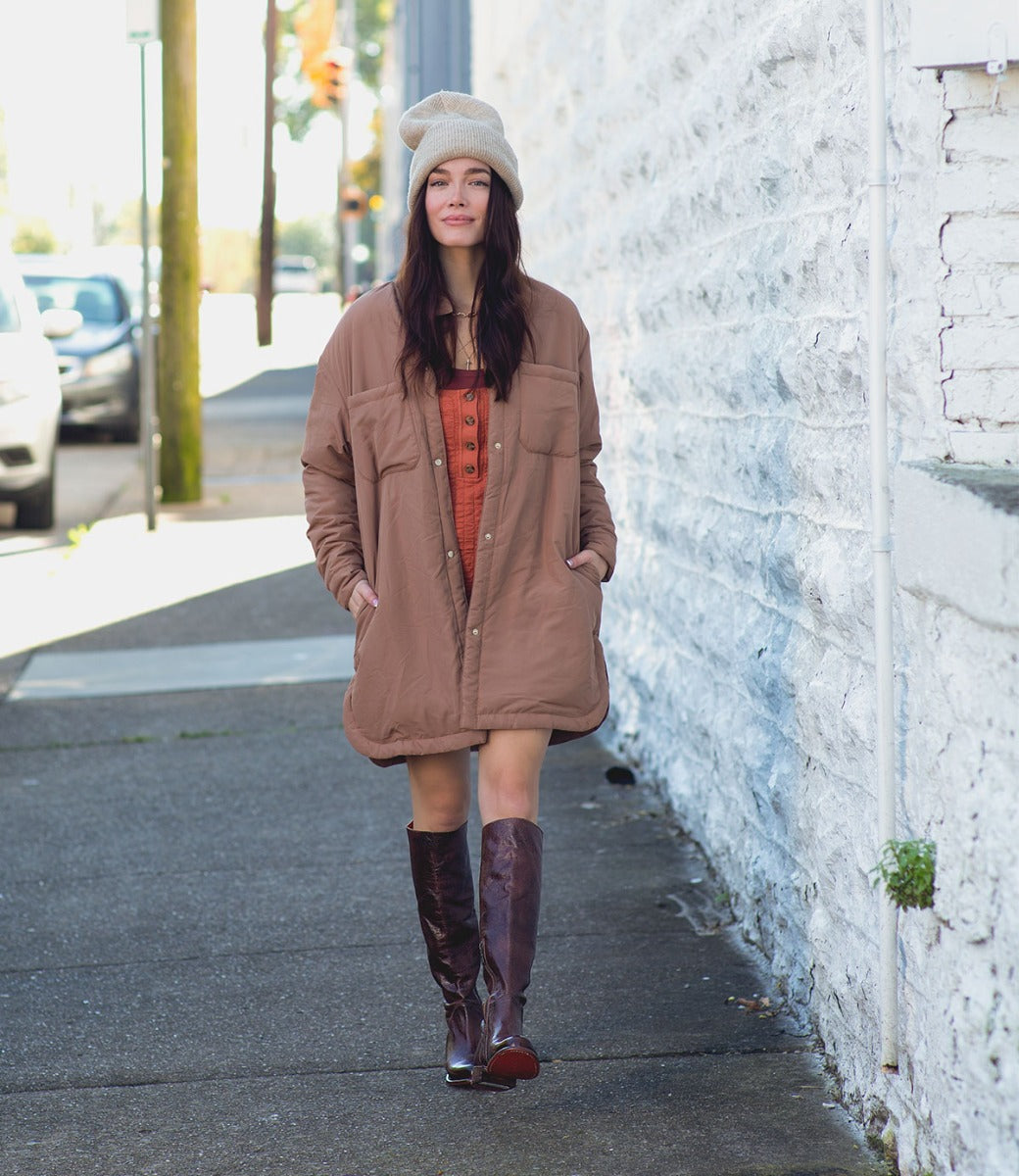 A woman in a brown coat and Bed Stu boots walking down a sidewalk.