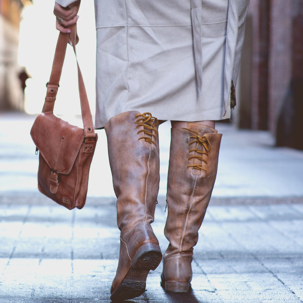 A woman in a Manchester Wide Calf trench coat and Bed Stu knee high boots walking down the street.