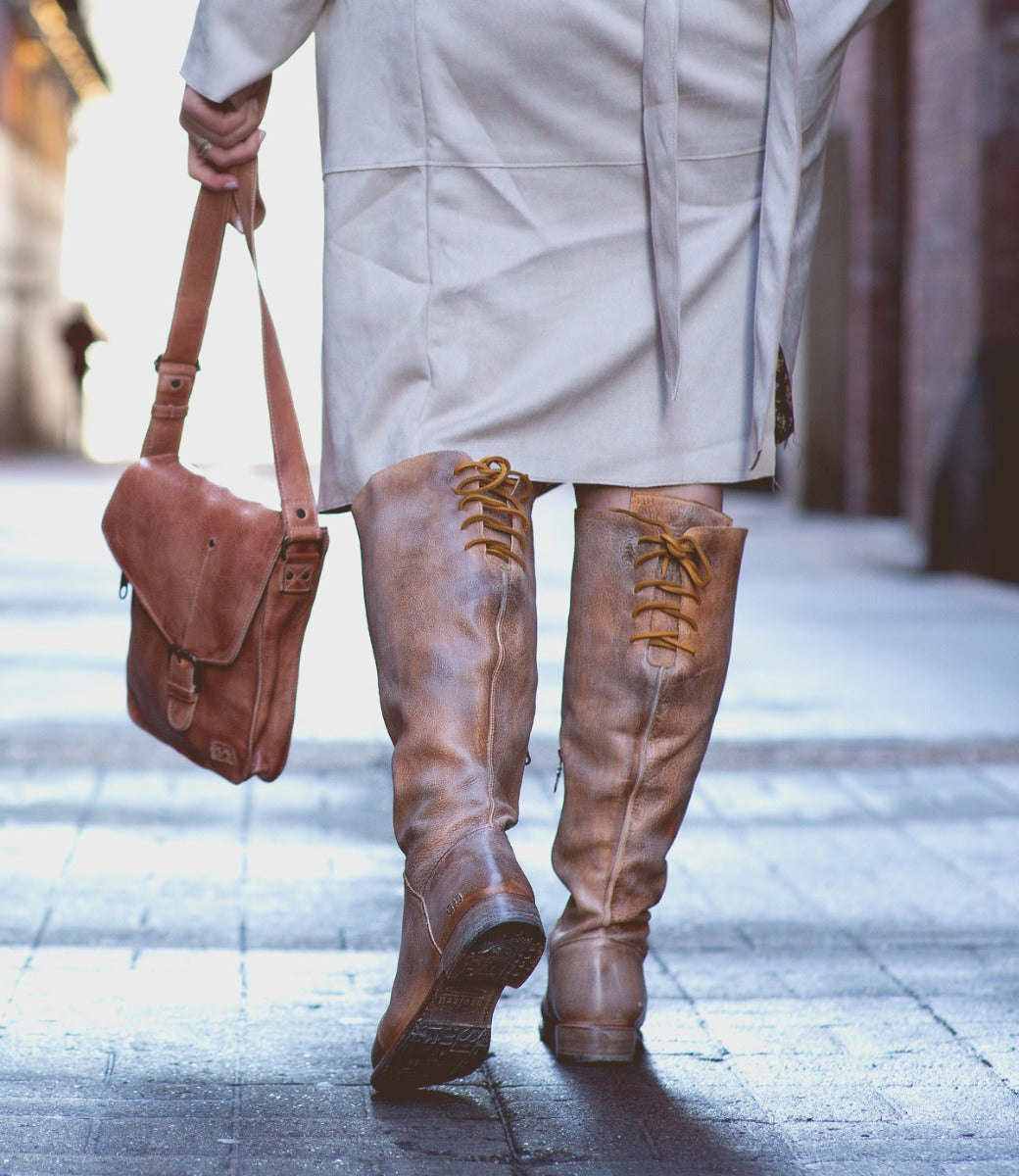 A woman in a Manchester Wide Calf trench coat and Bed Stu knee high boots walking down the street.