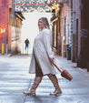 A woman in a beige Bed Stu coat walking down an alley.