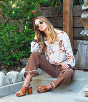 A woman is sitting on the steps wearing a brown Marie sandals by Bed Stu.