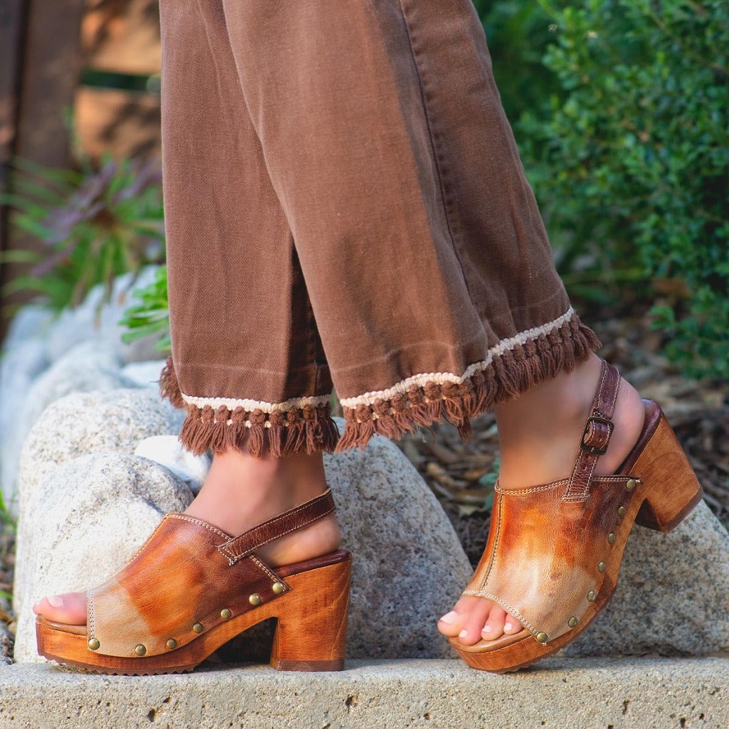 A woman wearing brown pants and Marie sandals by Bed Stu.