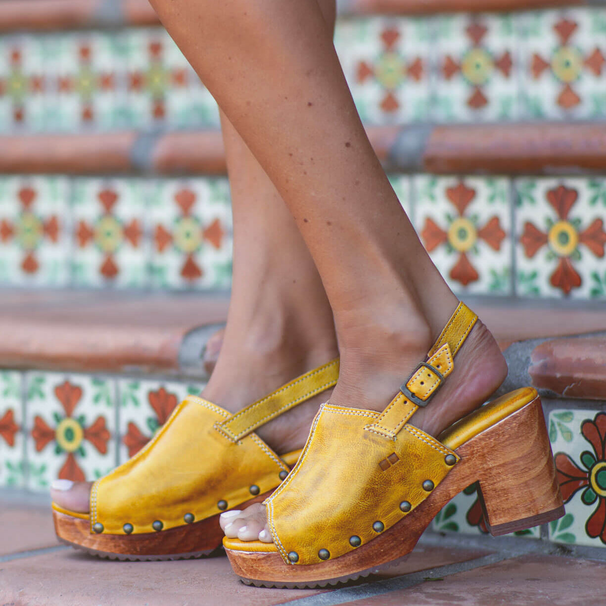 A woman wearing yellow Bed Stu Marie sandals on a set of steps.