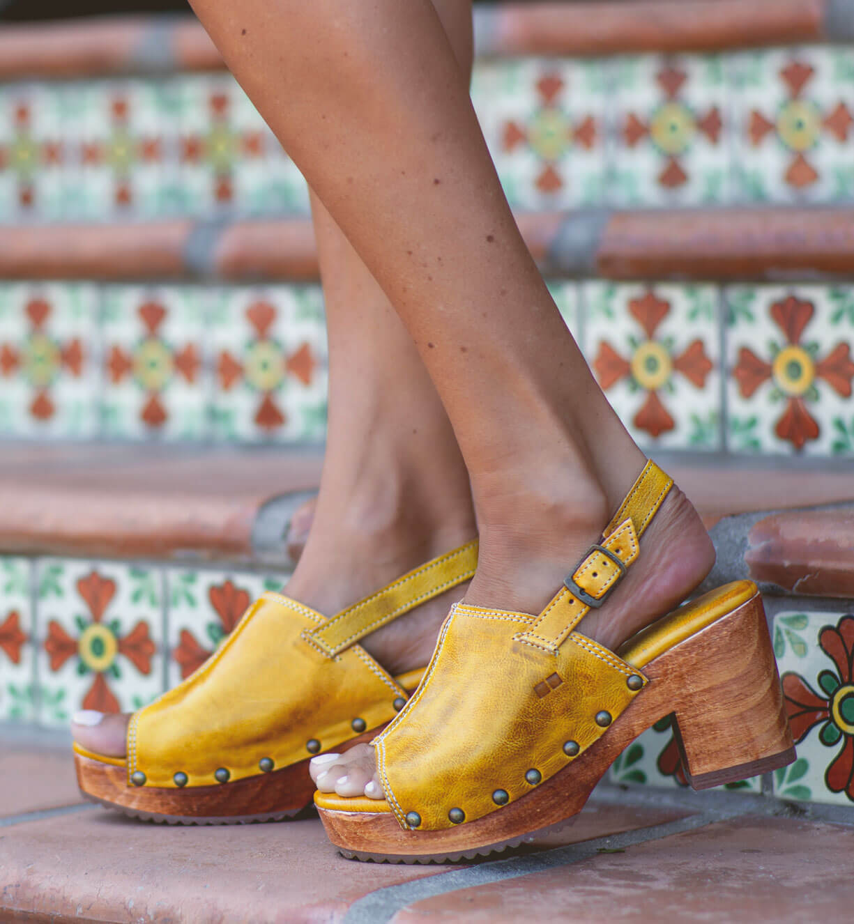 A woman wearing yellow Bed Stu Marie sandals on a set of steps.