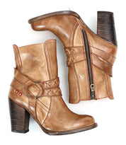 A brown leather heeled pair of boots with o-ring harness, red stitching accents on the profile view. 