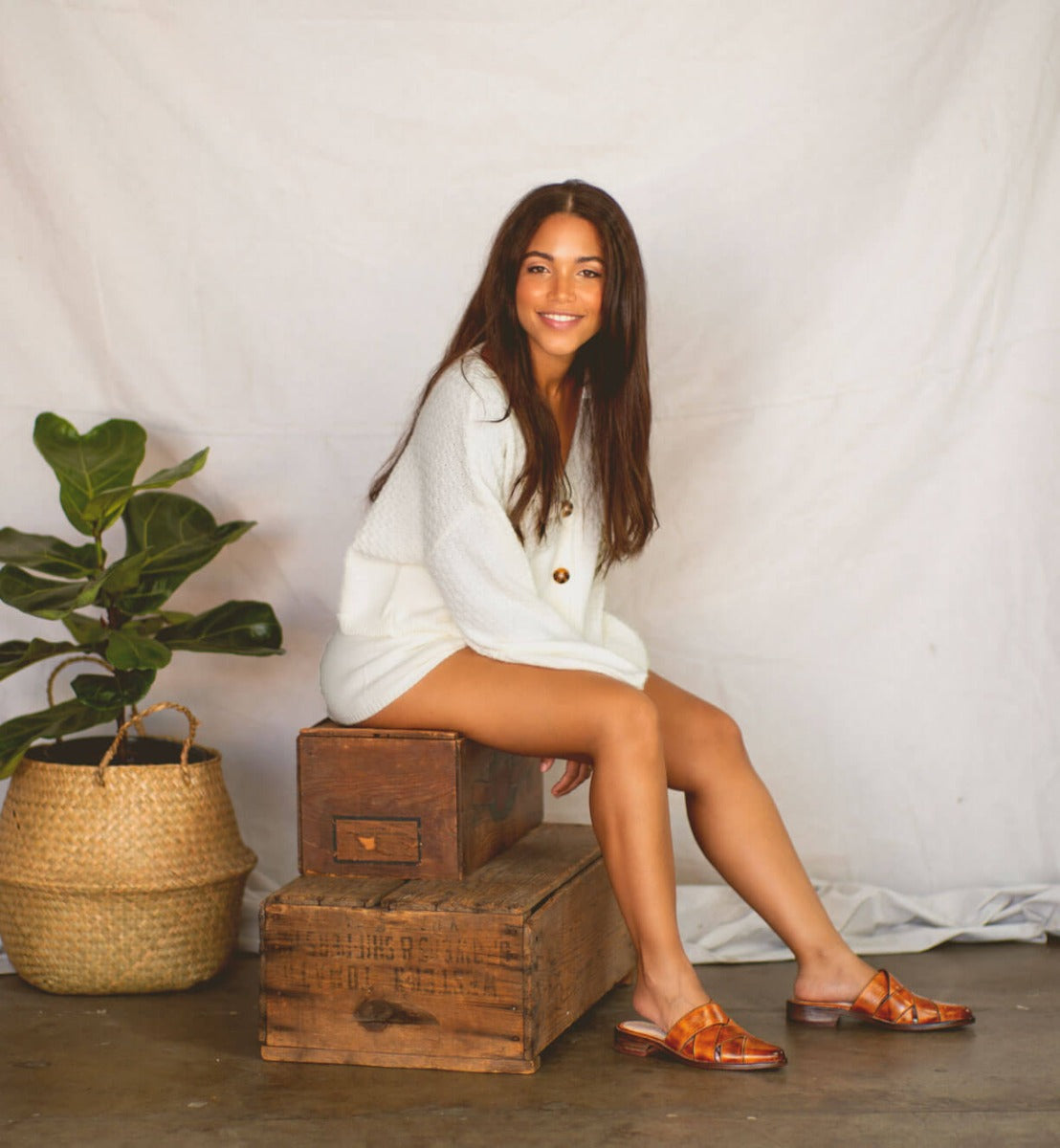 A woman in a white Mayra sweater sitting on a wooden box.