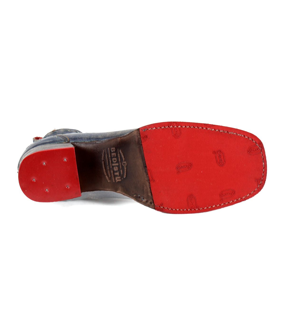 The image showcases the Merryli shoe by Bed Stu, featuring a distinctive red bottom sole with the brand's logo engraved in the middle. Made from eco-friendly materials, the heel area is adorned with three small, round metal studs, while a cushioned insole ensures all-day comfort.