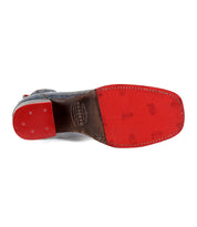 The image showcases the Merryli shoe by Bed Stu, featuring a distinctive red bottom sole with the brand's logo engraved in the middle. Made from eco-friendly materials, the heel area is adorned with three small, round metal studs, while a cushioned insole ensures all-day comfort.
