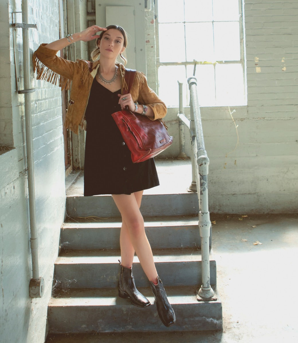 A woman wearing a Merryli black dress and a Bed Stu tan jacket standing on stairs.