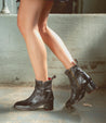 The legs of a woman wearing Bed Stu Merryli black leather ankle boots.