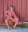 A woman sitting on a chair in a Bed Stu red striped Merryli jumpsuit.