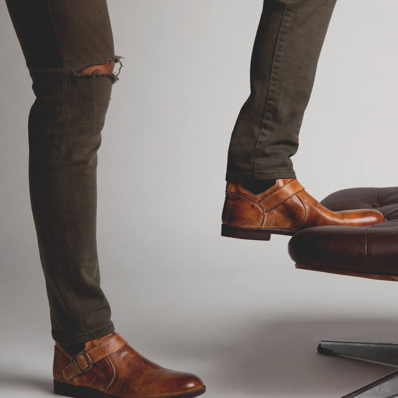 A man standing on a chair wearing Bed Stu Michelangelo brown leather shoes.