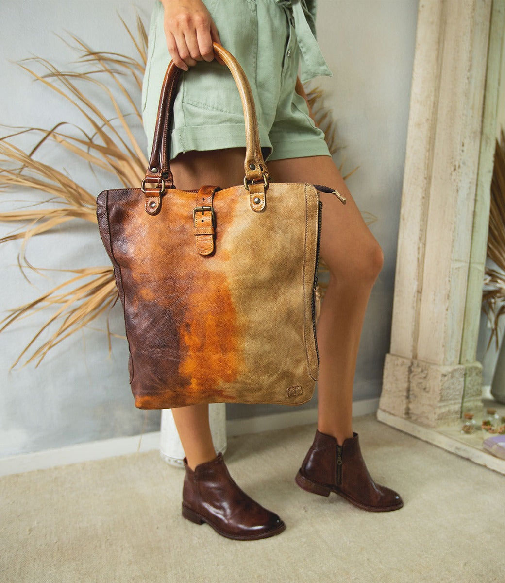 A woman holding a Bed Stu Mildred brown leather tote bag.