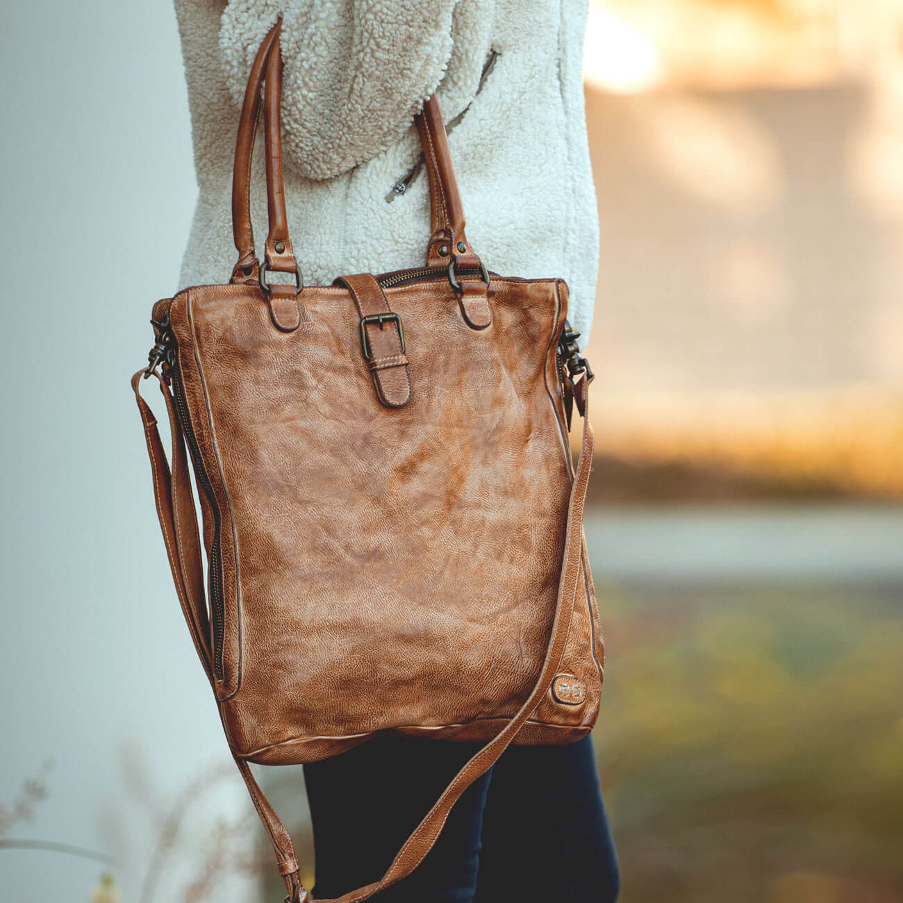 A woman holding a Bed Stu Mildred brown leather tote bag.